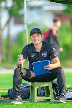 Smiling sports coach holding a microphone and clipboard outdoors in Hanoi.