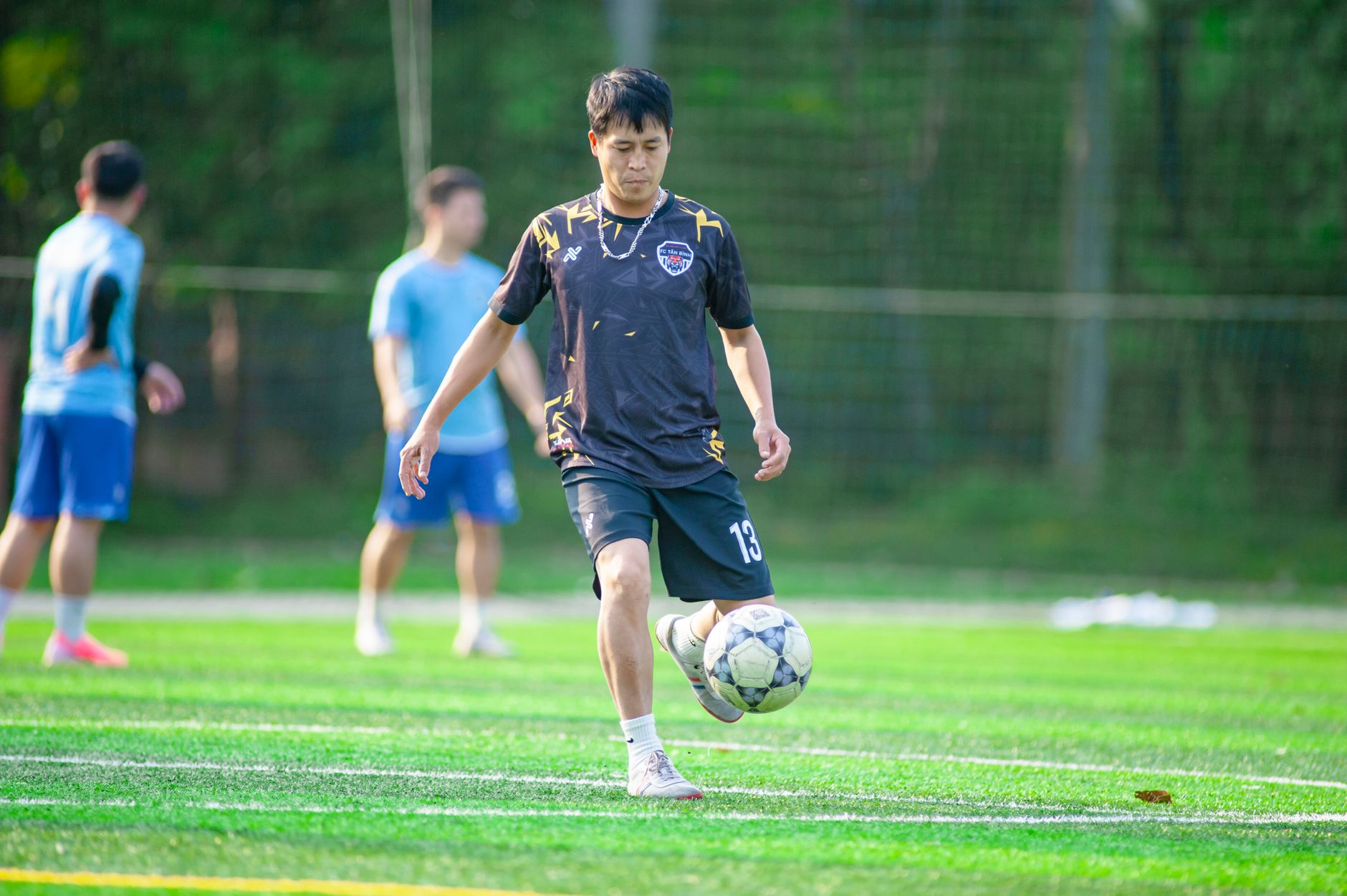 Group of young men playing soccer on a vibrant green field in Hanoi, Vietnam.