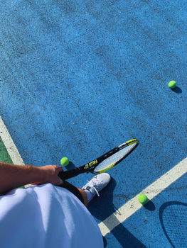 Top-down view of a tennis player on a blue court with racket and balls, ready to play.
