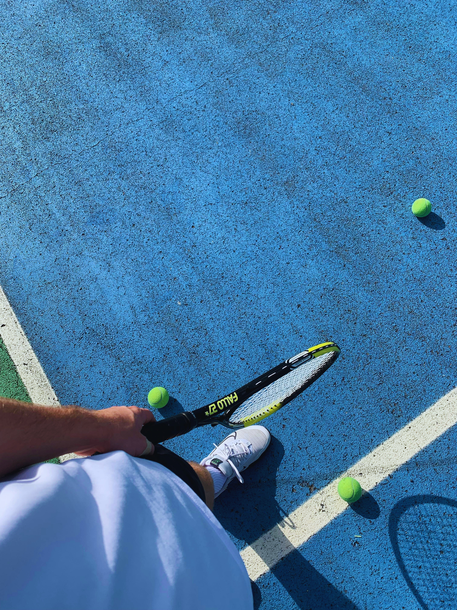 Tennis player standing on a blue court with racket and tennis balls