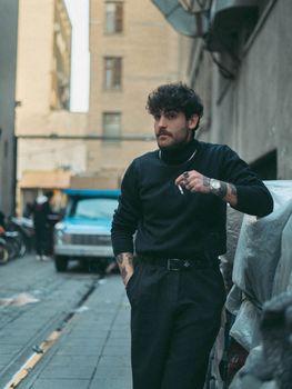 Young man with tattoos posing in an urban alley with a vintage car.