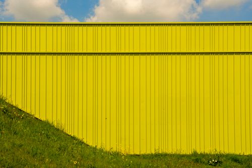 Free Bright yellow corrugated metal wall with grassy foreground under a clear blue sky. Stock Photo