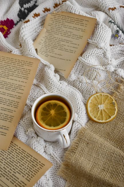 A warm cup of lemon tea and vintage book pages on a knit blanket create a perfect cozy atmosphere.