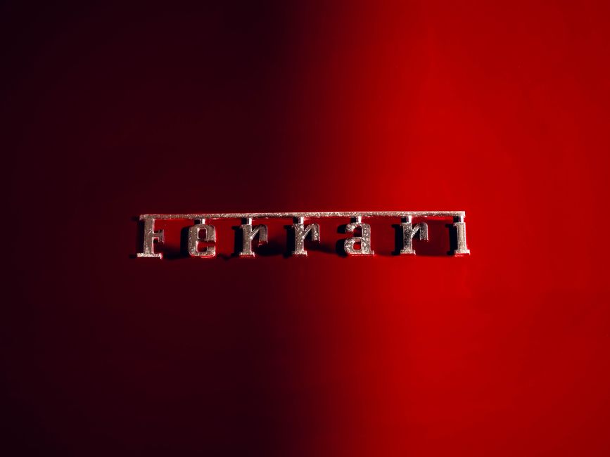 Detailed shot of a Ferrari emblem on a sleek red background, showcasing luxury automotive design.