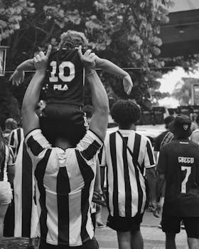 Fans in striped jerseys celebrate a soccer event outdoors, in dynamic black and white.