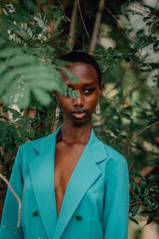 Stylish woman in a green blazer standing among lush greenery outdoors, exuding elegance.