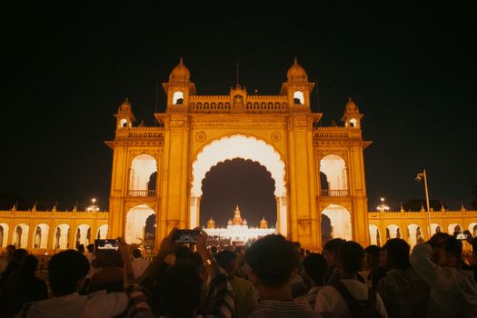 Illuminated Mysore Palace entrance bustling with people at night, capturing vibrant architecture.