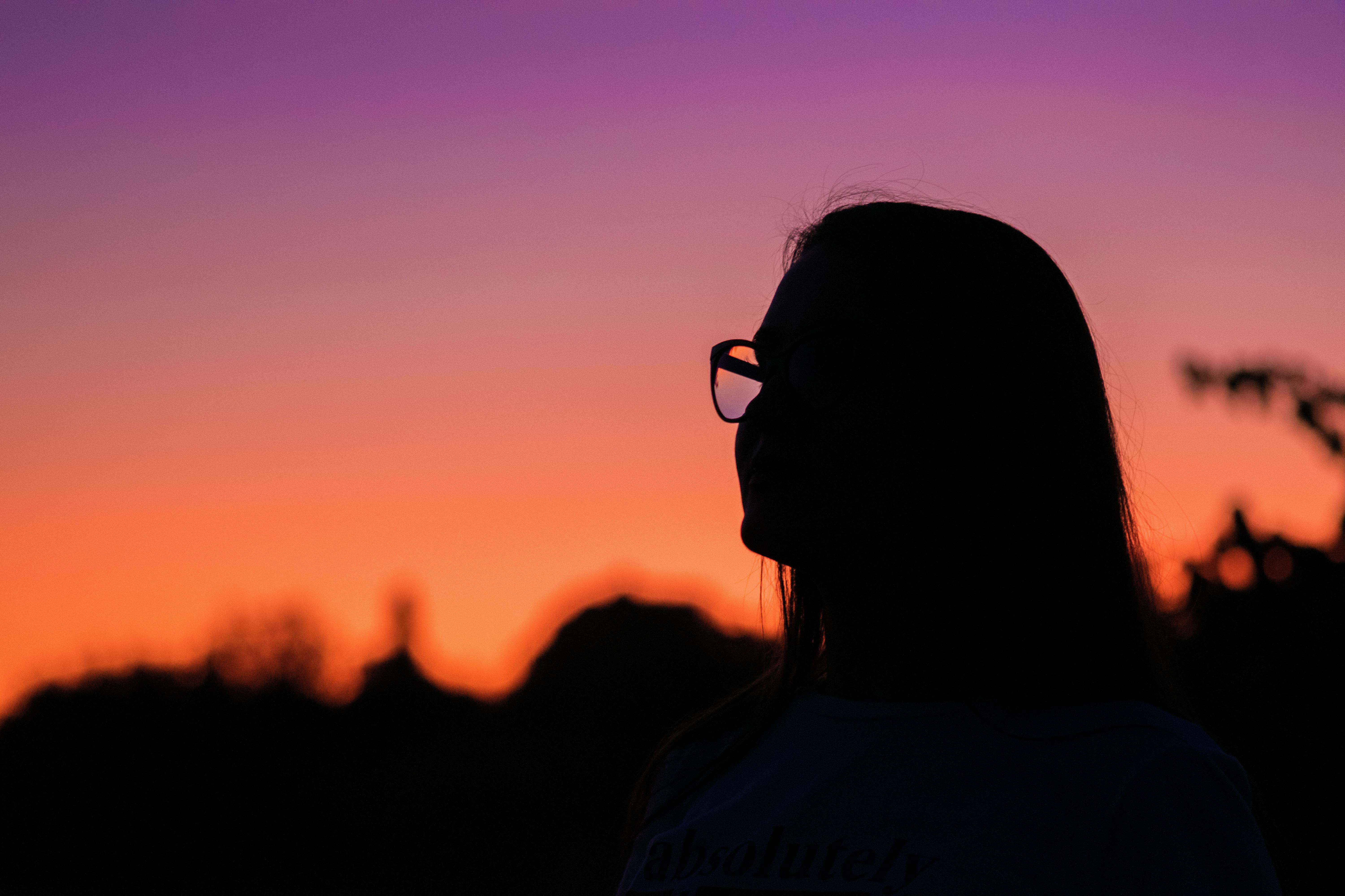 一个戴眼镜的人的剪影映衬在生动的橙紫色日落中