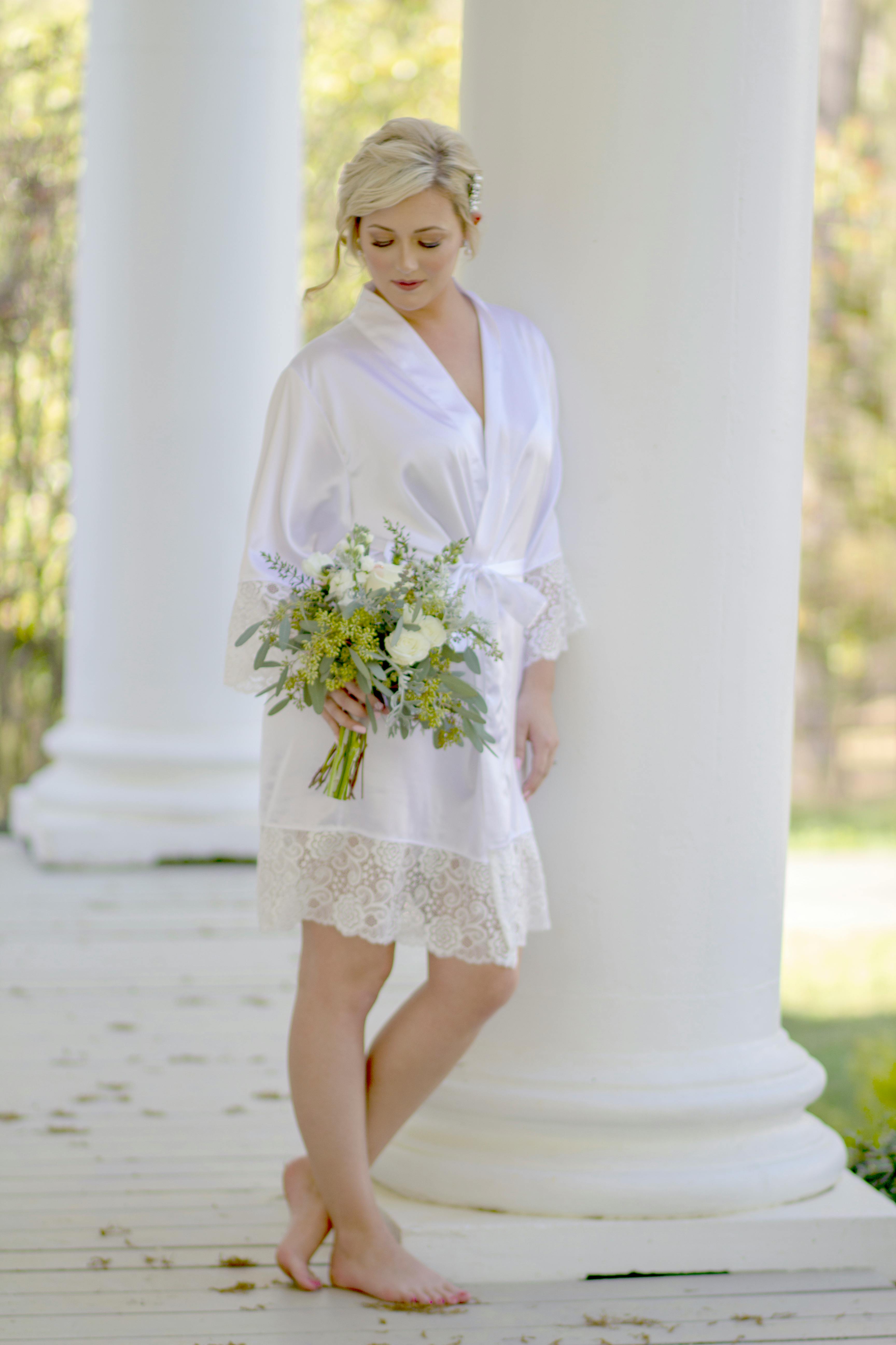 在宁静的户外环境中，一位美丽的白衣新娘手持花束，正在拍摄