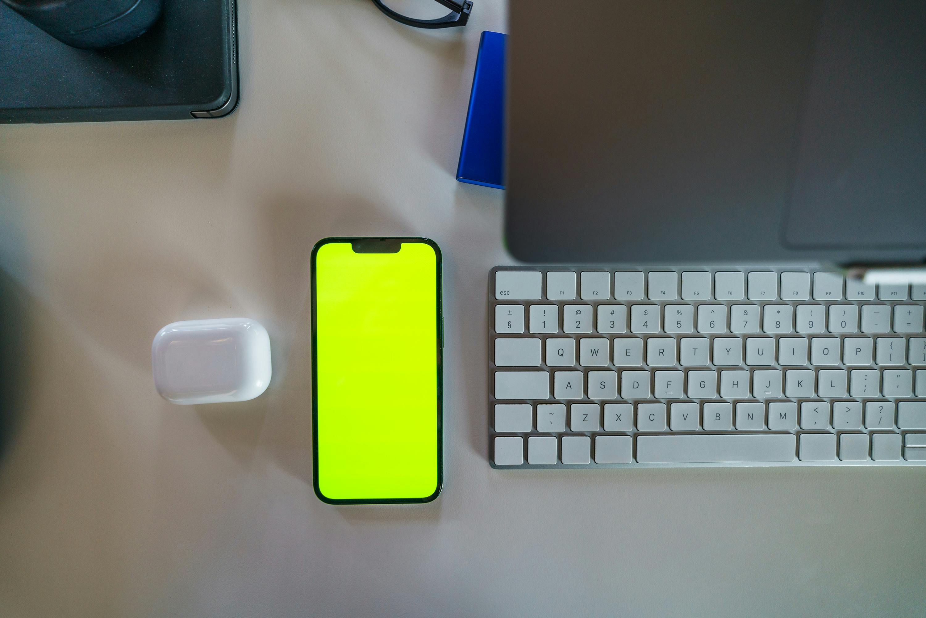 Ücretsiz Yeşil ekranlı akıllı telefon, dizüstü bilgisayar ve klavyenin yer aldığı modern bir çalışma alanının yukarıdan görünümü. Stok Fotoğraflar