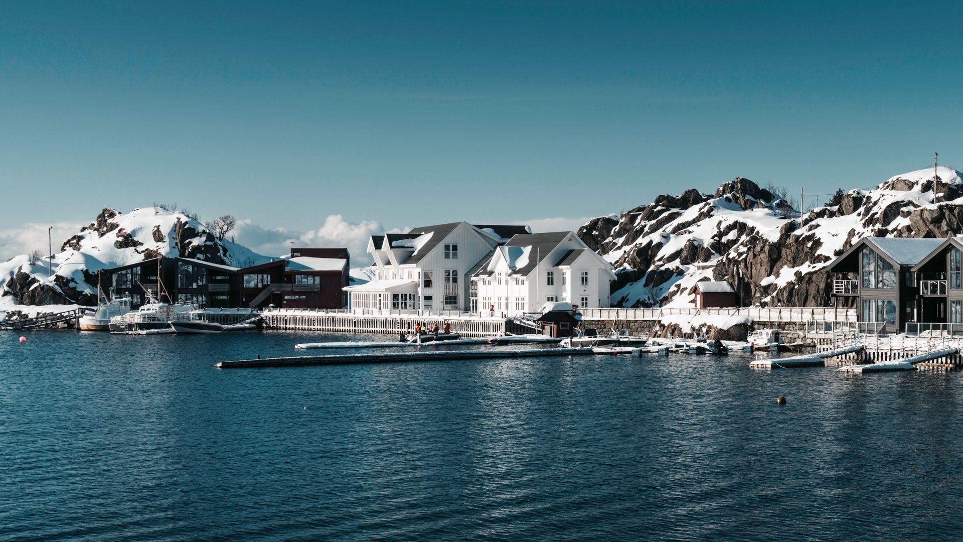 Explore a serene Arctic fjord resort surrounded by snow-covered mountains, showcasing tranquil beauty.