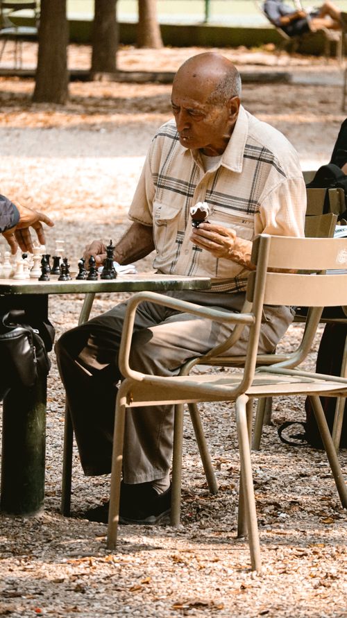 Free Senior man playing chess and eating ice cream in a park setting, capturing leisure and strategy. Stock Photo