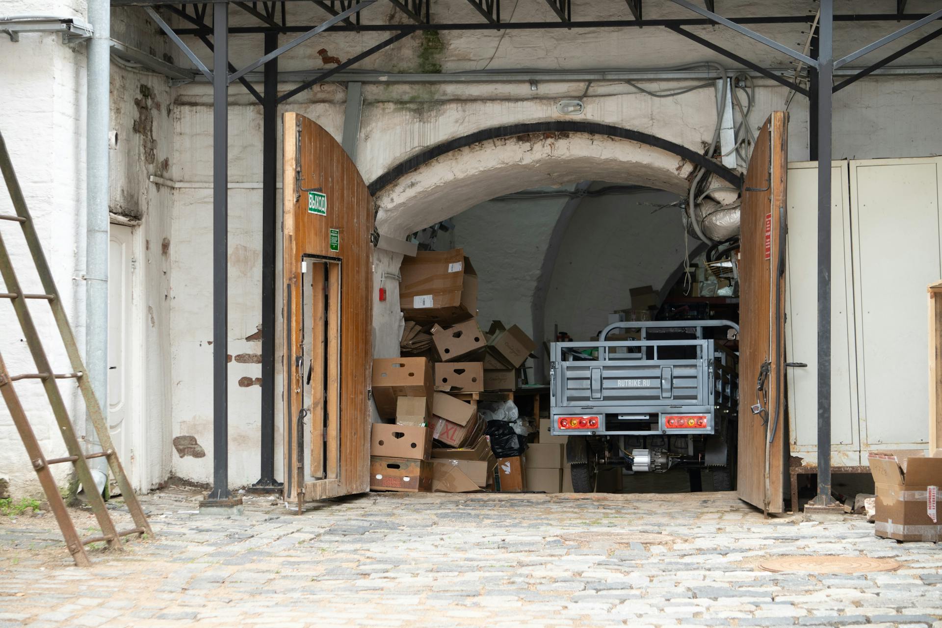 Warehouse entrance with cardboard boxes and open wooden doors, a vehicle partially visible.