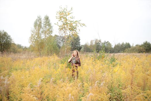 Woman in a yellow meadow, holding flowers, enjoying a bright autumn day outdoors.