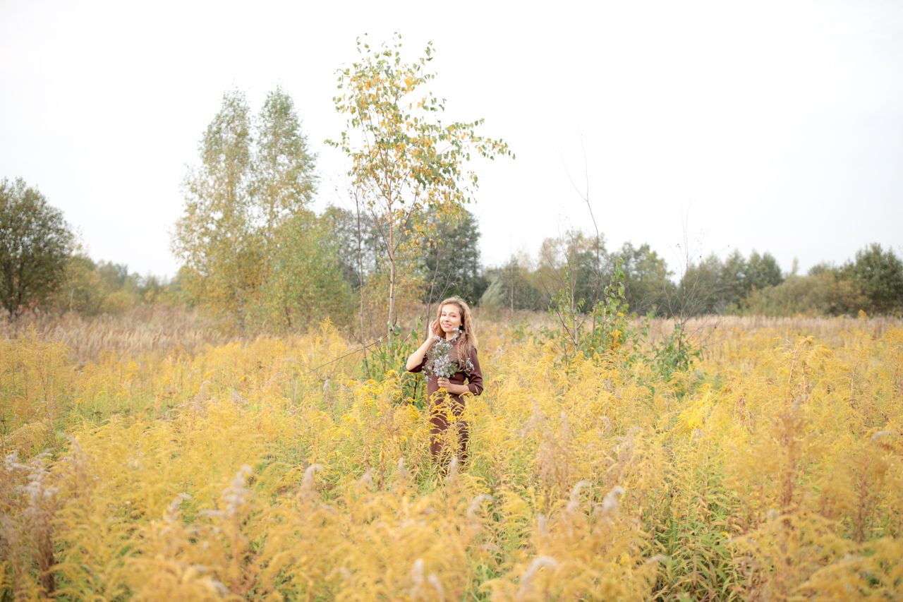 woman in a yellow meadow holding flowers enjoying a bright autumn day