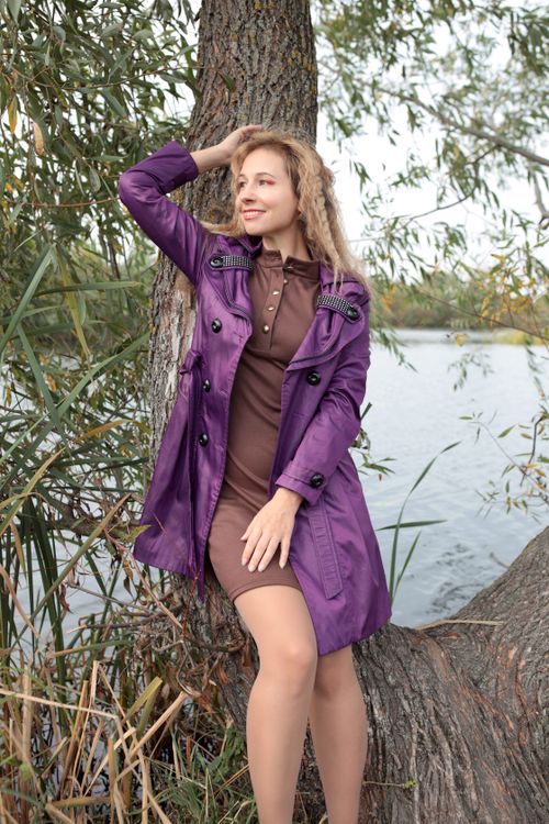 Free Elegant woman in a purple coat posing by a tree near a lake during autumn. Stock Photo