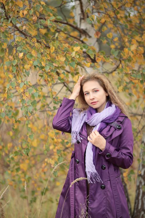 Free Woman in a purple coat and scarf posing outdoors in fall foliage. Stock Photo