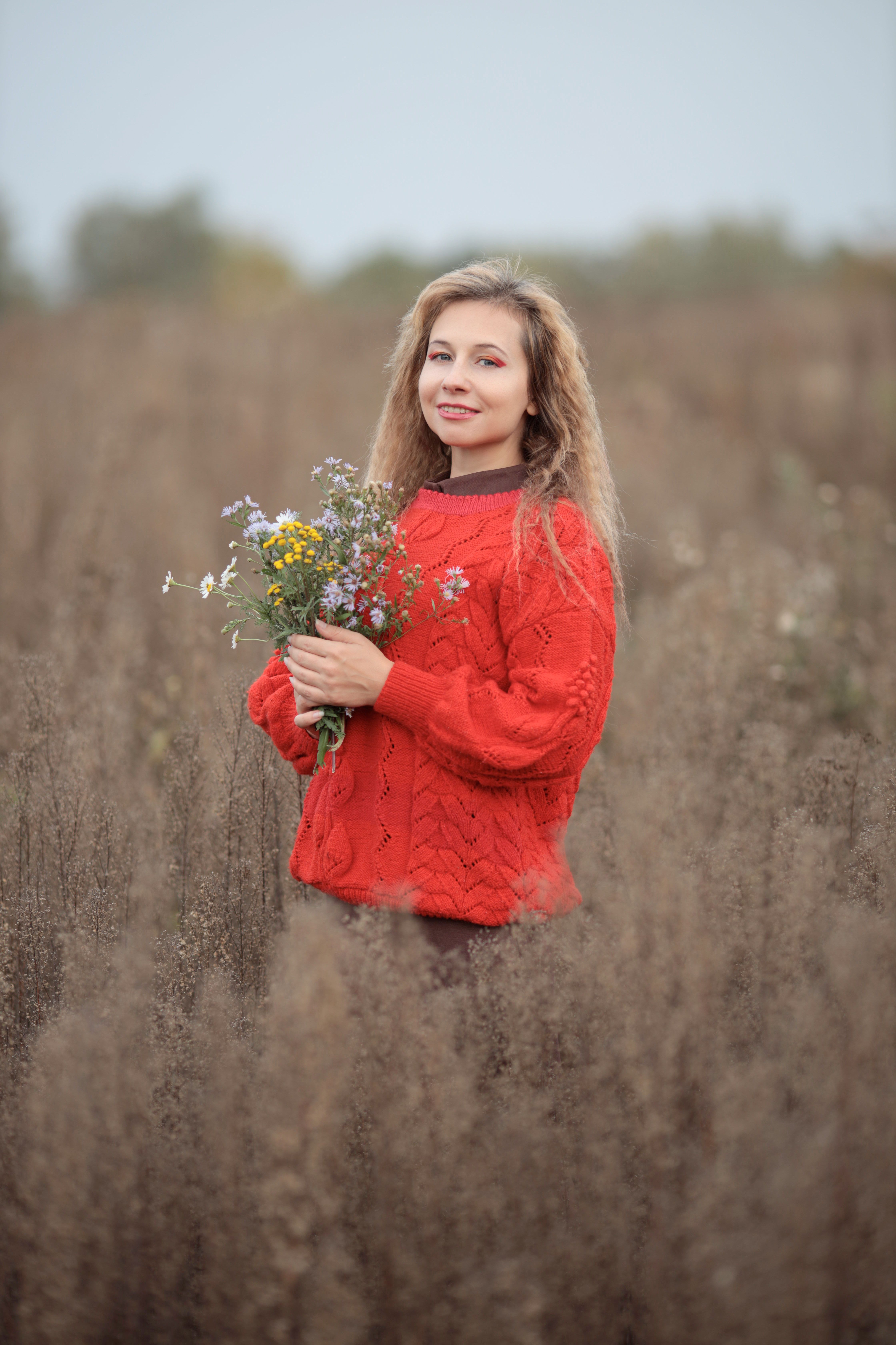 Woman in Red Sweater Holding Wildflowers Outdoors · Free Stock Photo