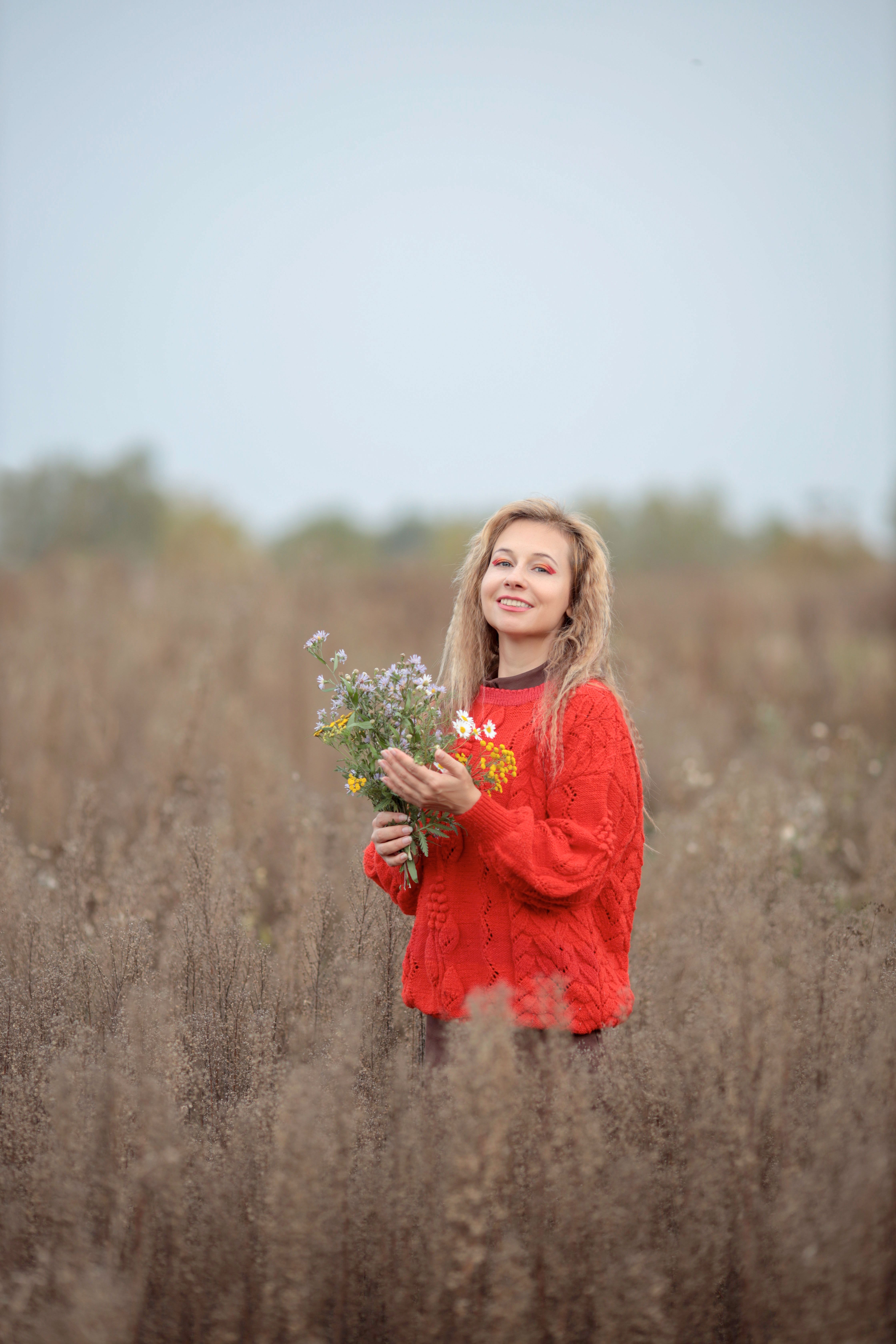 Woman in Red Sweater Holding Flowers in Meadow · Free Stock Photo