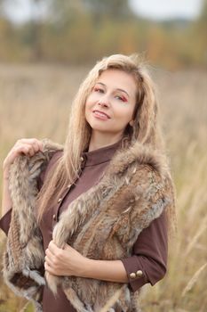 Blonde woman wearing a fur vest enjoying the outdoors during autumn, smiling warmly.