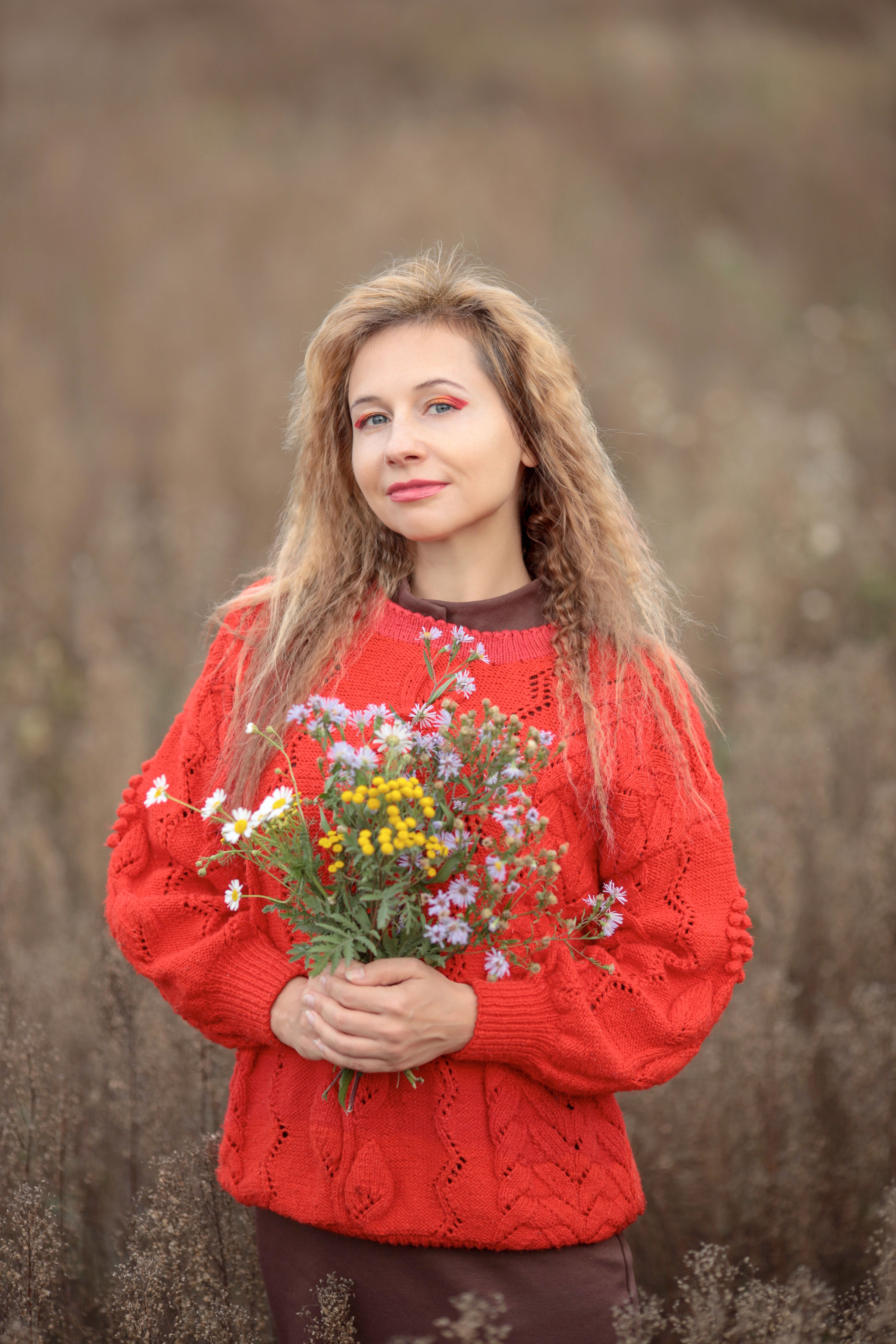 Woman in Red Sweater Holding Wildflowers Outdoors · Free Stock Photo