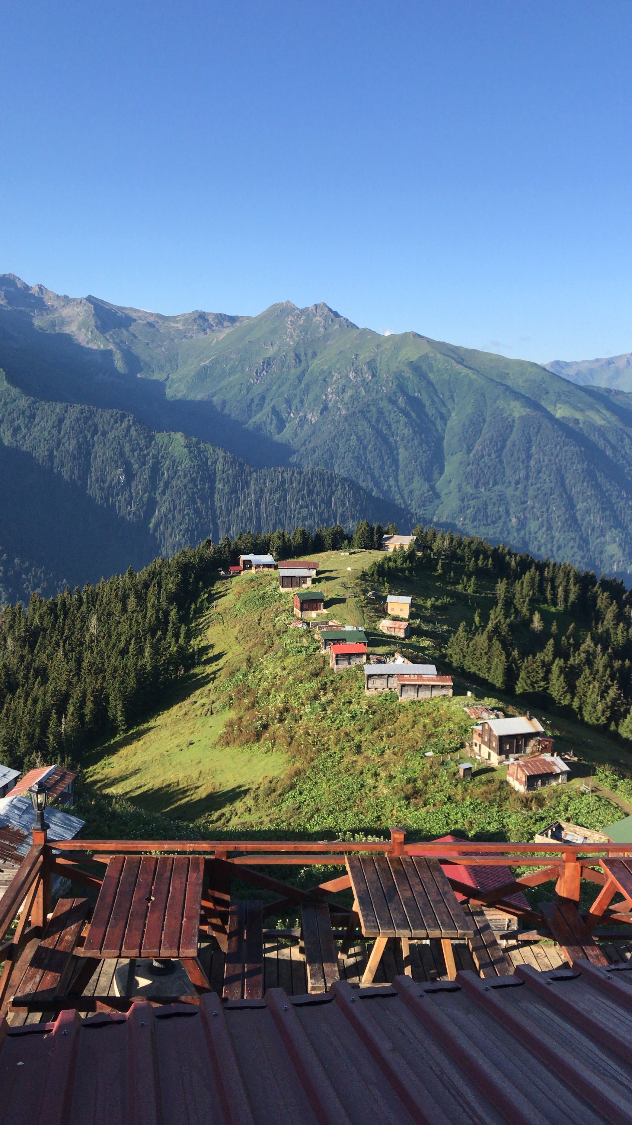 A stunning view of mountain village houses on a ridge surrounded by lush greenery and towering peaks.