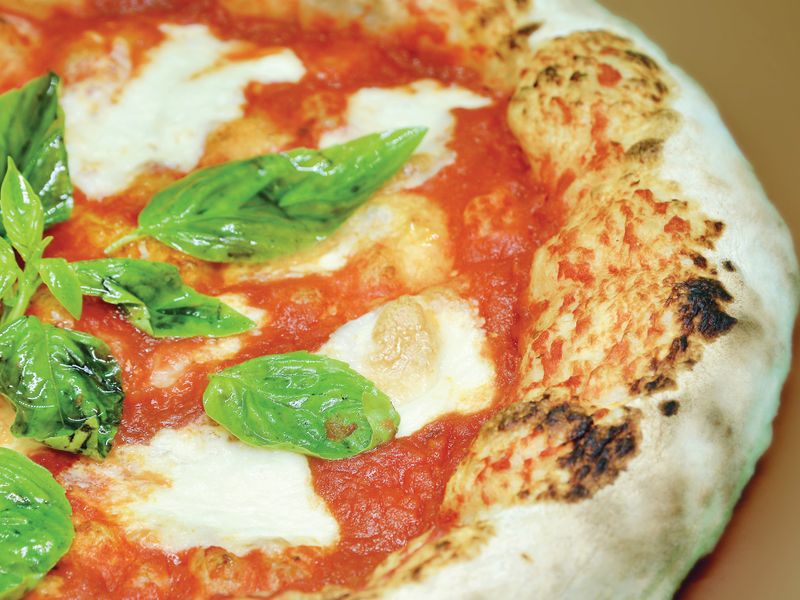 Close-up of a freshly baked Neapolitan pizza with mozzarella and basil leaves.