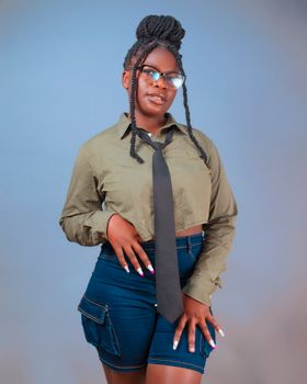 A young woman poses confidently in casual attire with glasses, braids, and a tie.