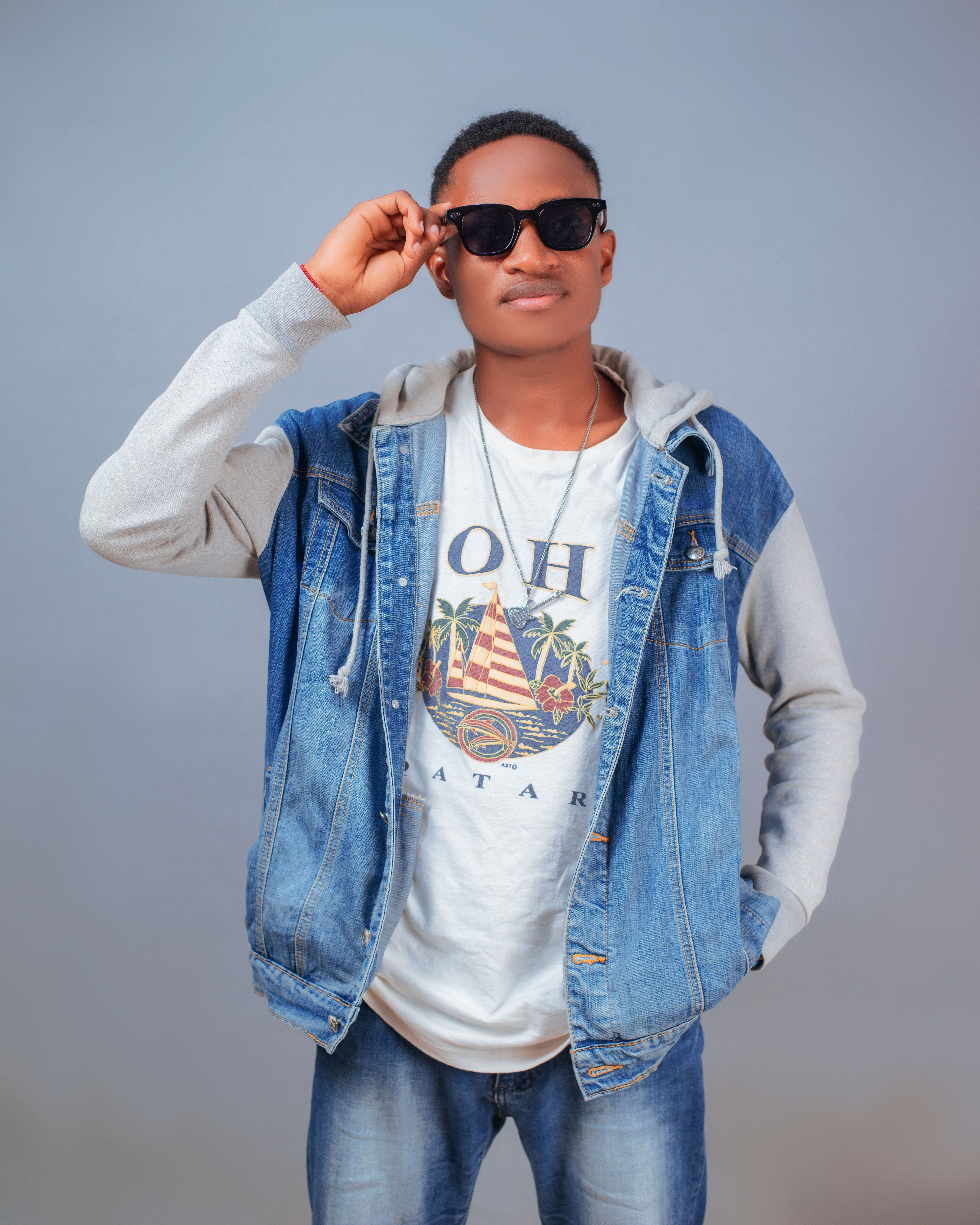 Portrait of a young man in casual denim and sunglasses against a neutral background.