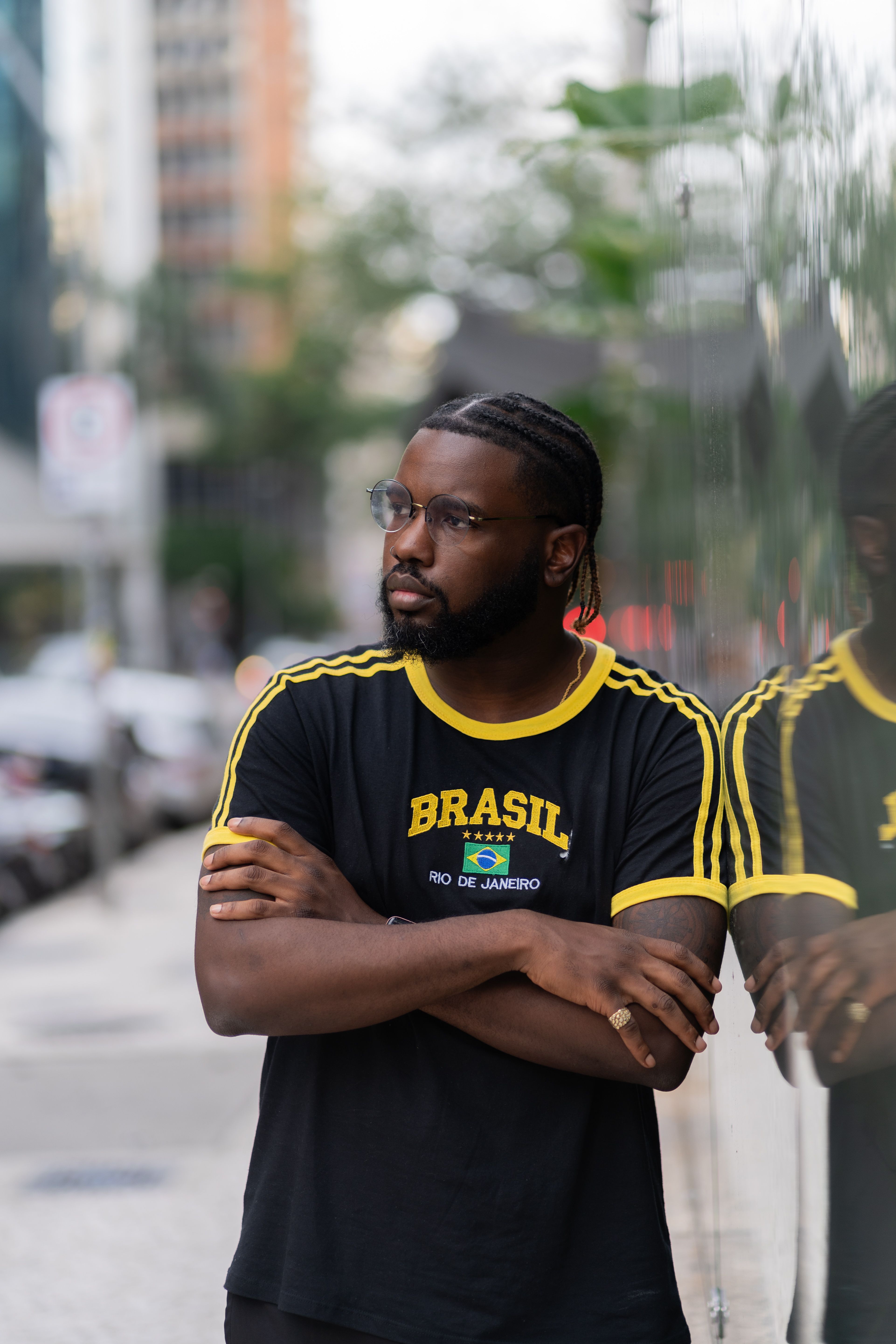 Man in a Brasil t-shirt stands by a reflective wall on a street in Rio de Janeiro, Brazil.
