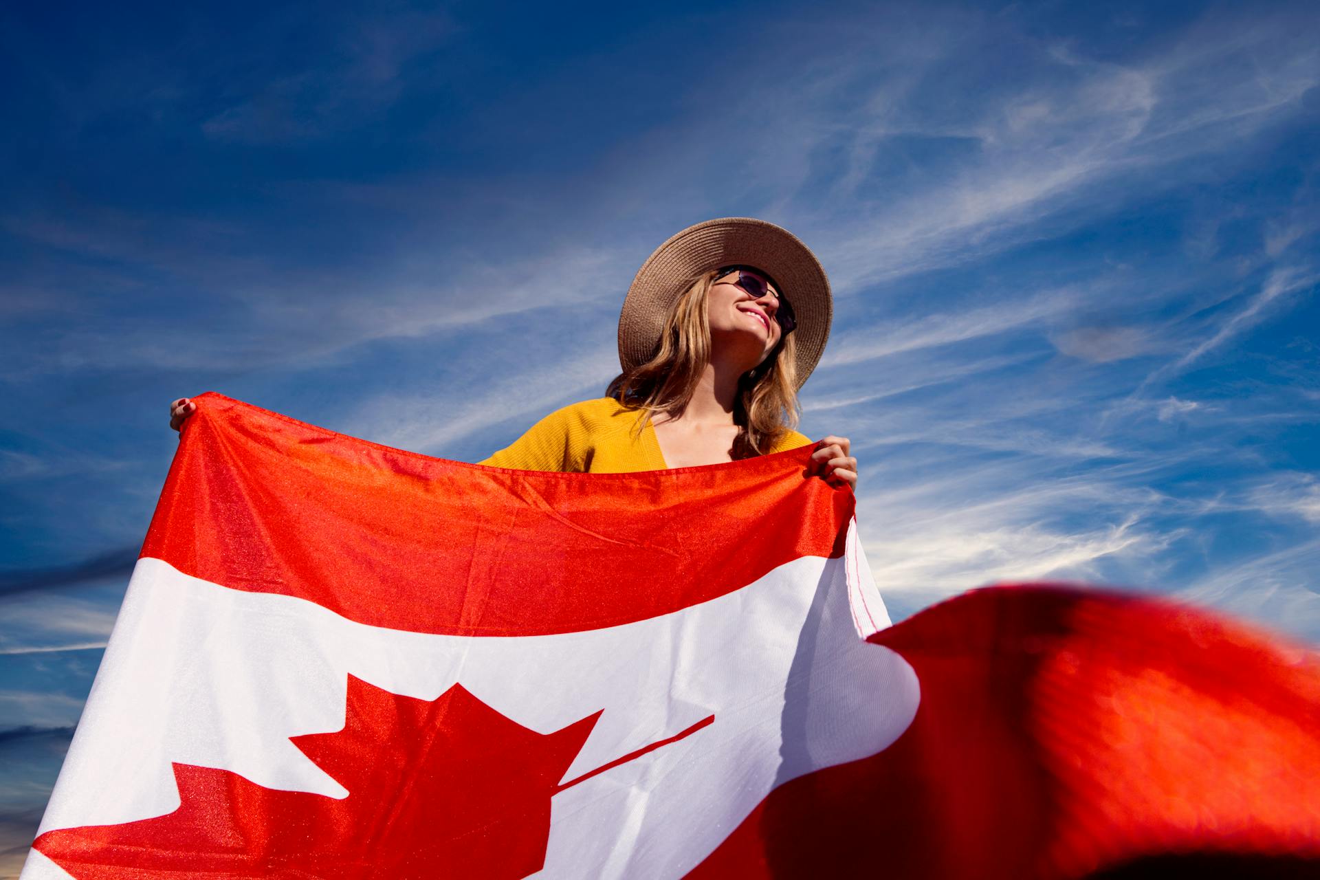 A joyful woman holding the Canadian flag under a clear blue sky, symbolizing national pride.