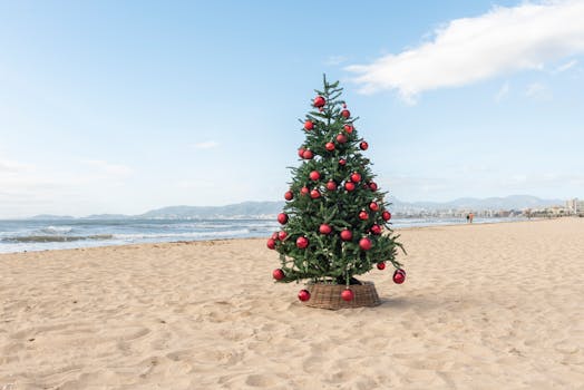 A vibrant Christmas tree with red ornaments stands on a sandy beach in Mallorca, blending holiday spirit with seaside tranquility.