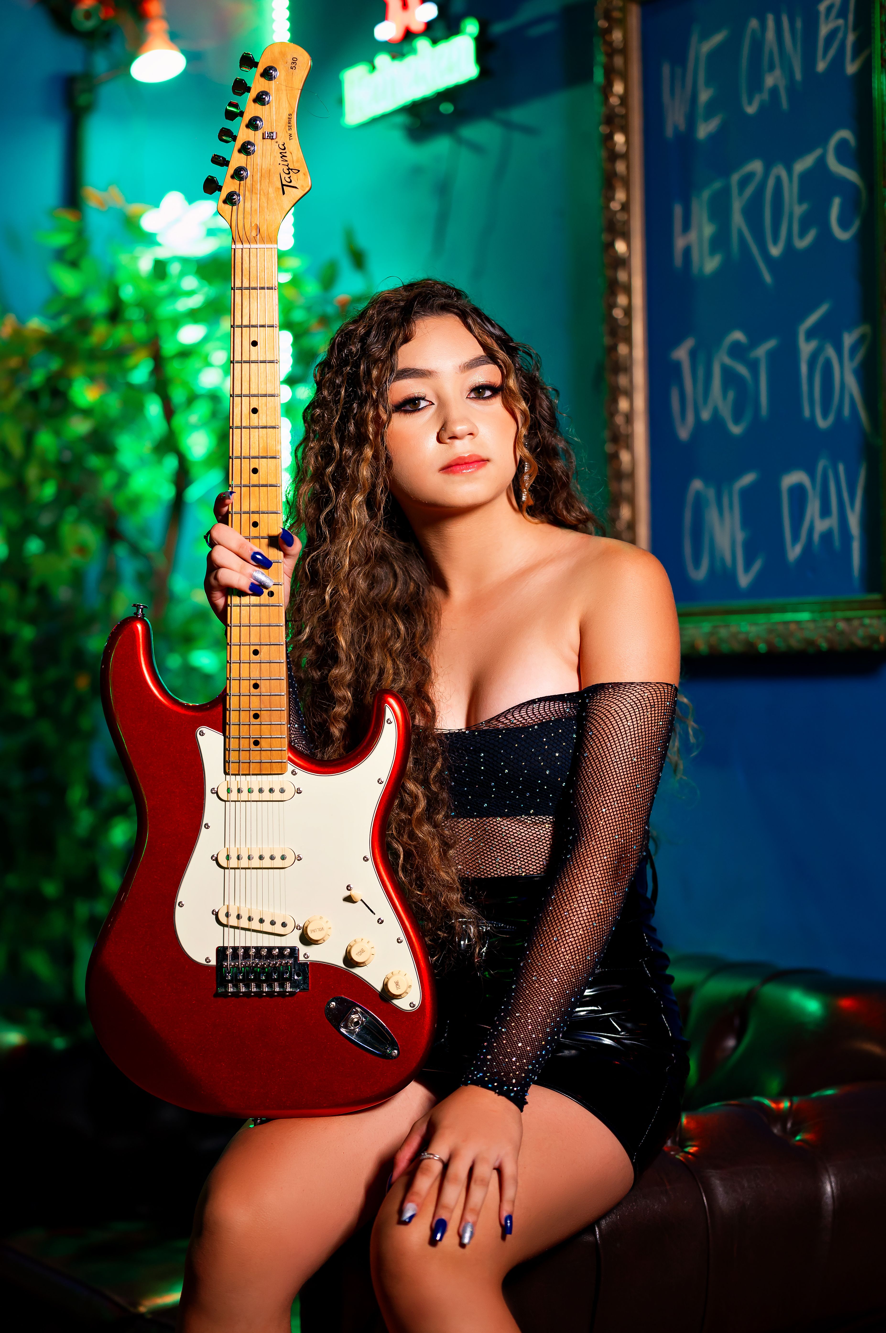 Glamorous young woman holding a red electric guitar in a vibrant lounge setting.