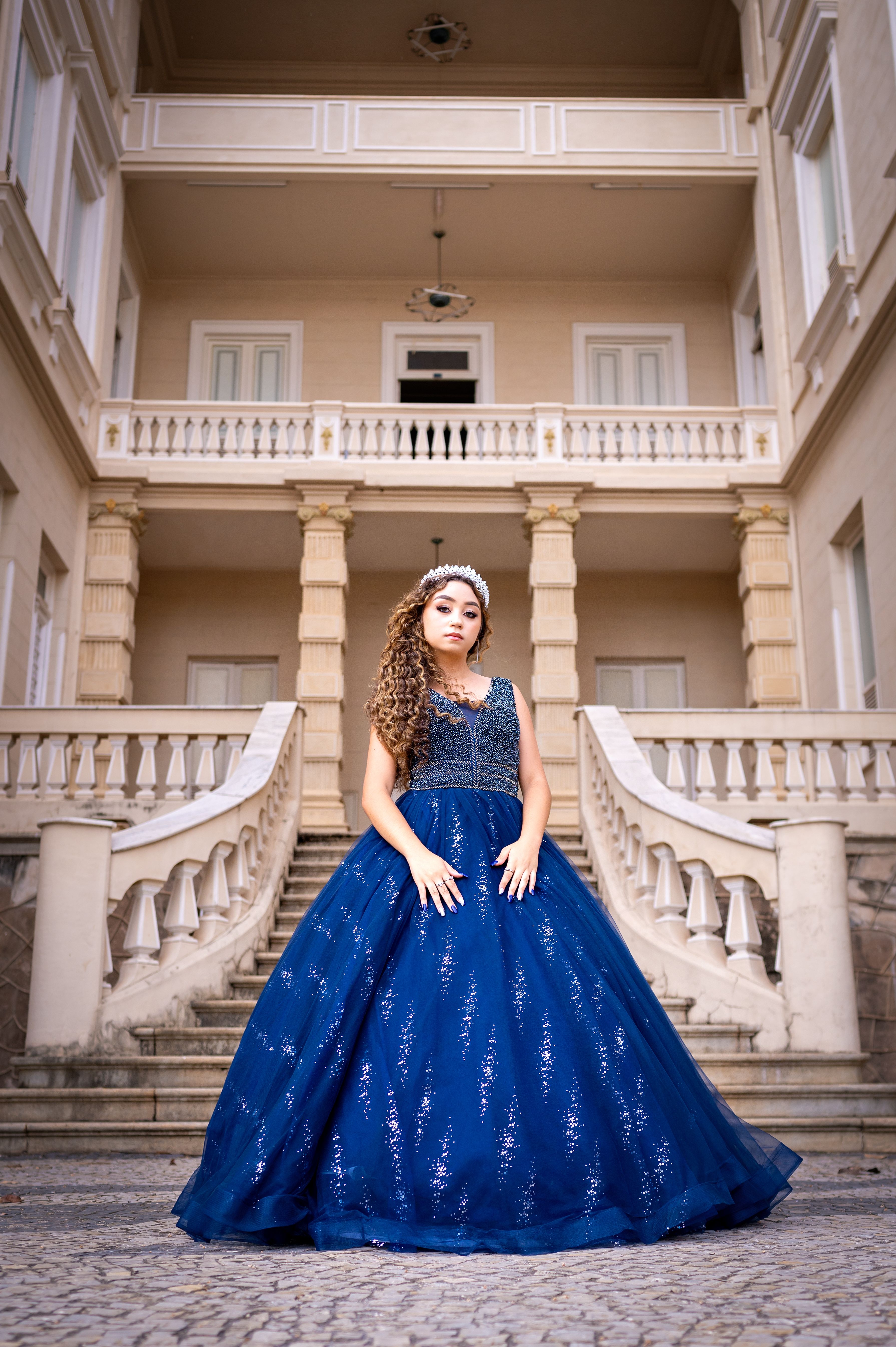 Portrait of a woman in a royal blue gown standing in front of a grand architectural structure.