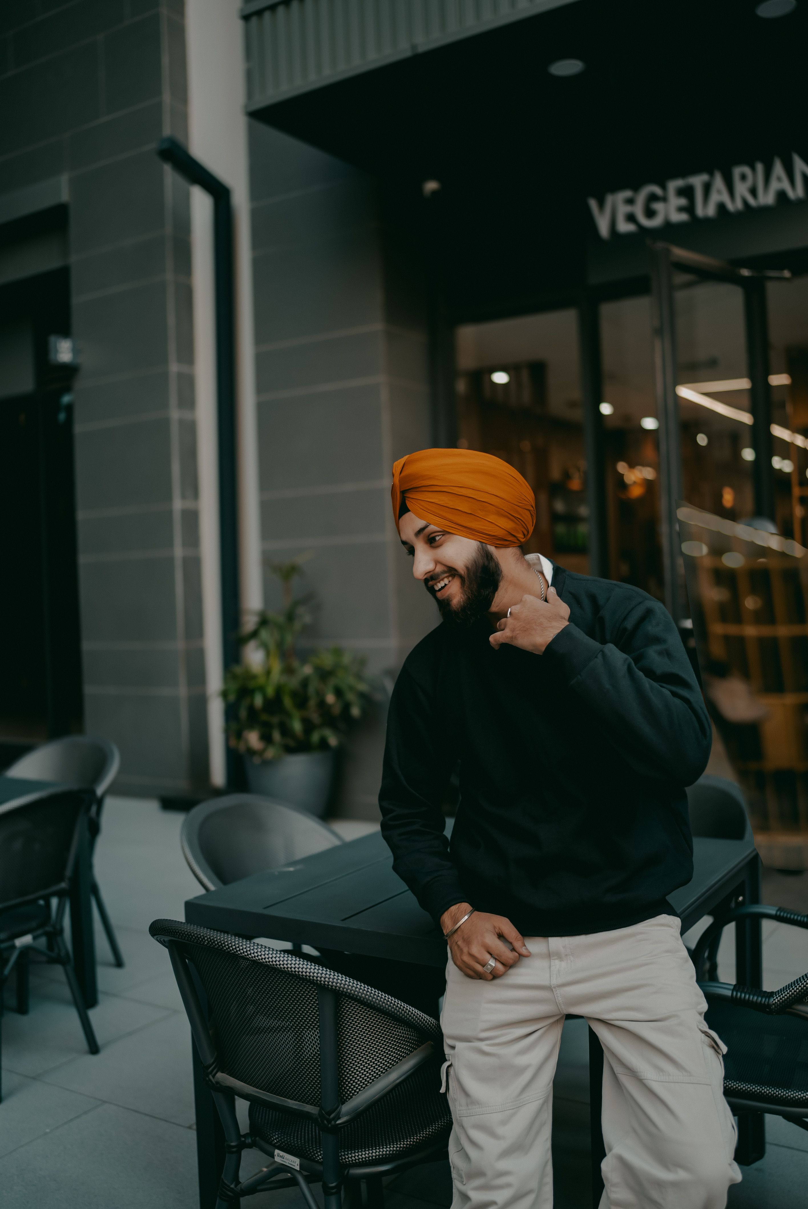 Cheerful man in orange turban enjoying a moment outside a vegetarian restaurant.