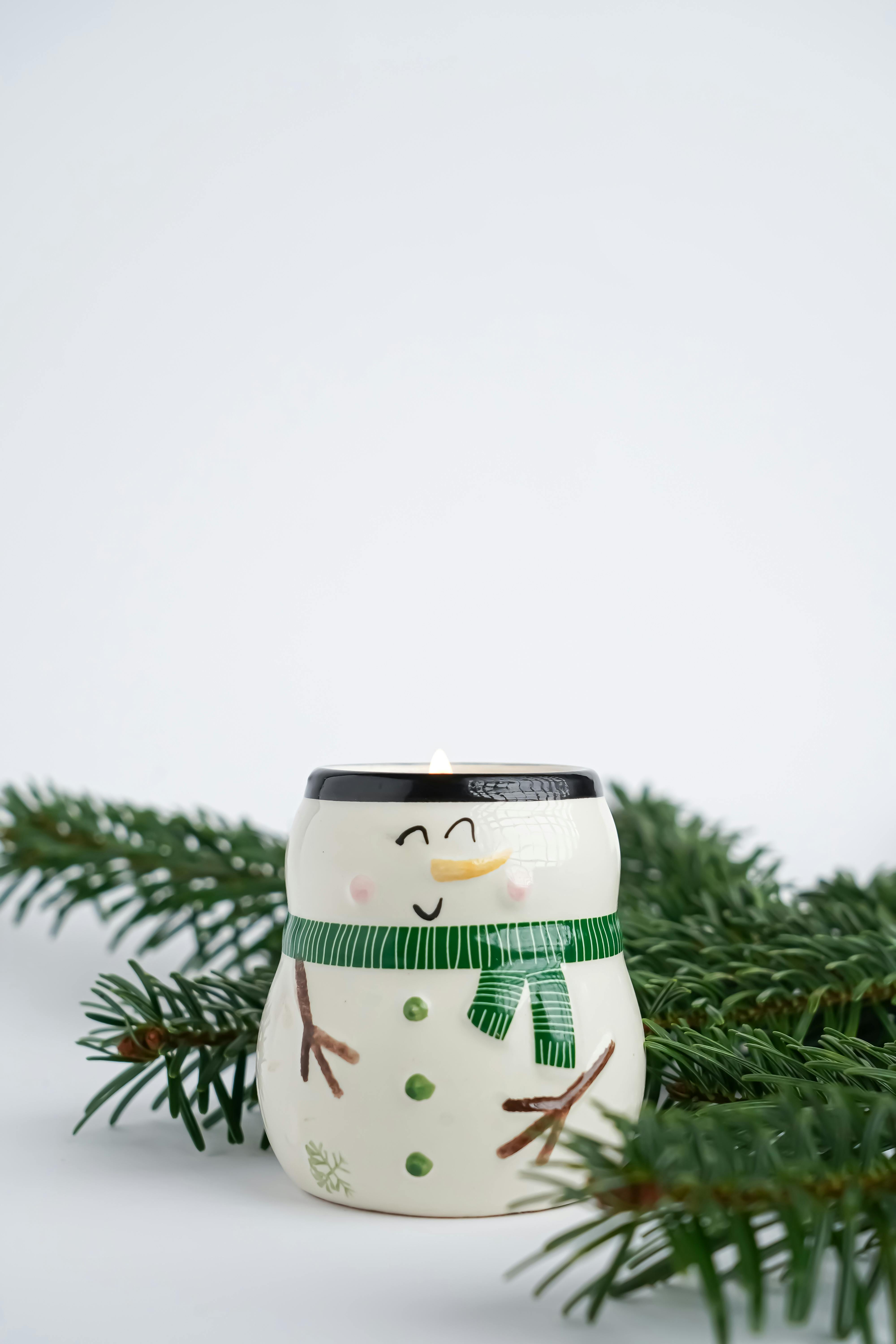 Snowman-themed candle surrounded by evergreen branches. Perfect for winter decor.
