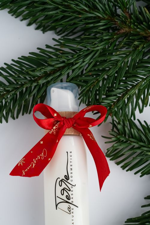 Free Christmas-themed vegan cosmetics bottle with red ribbon and evergreen branches. Stock Photo