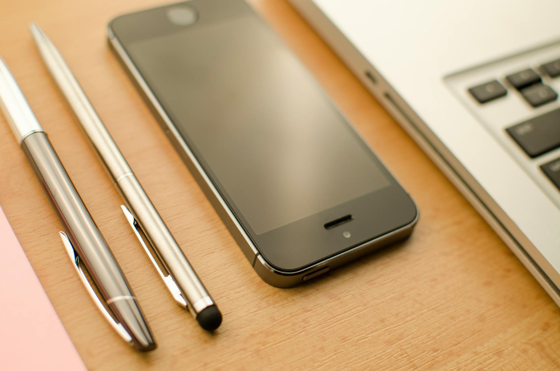 A neatly arranged desk featuring a smartphone, laptop, and pens in an office setting.