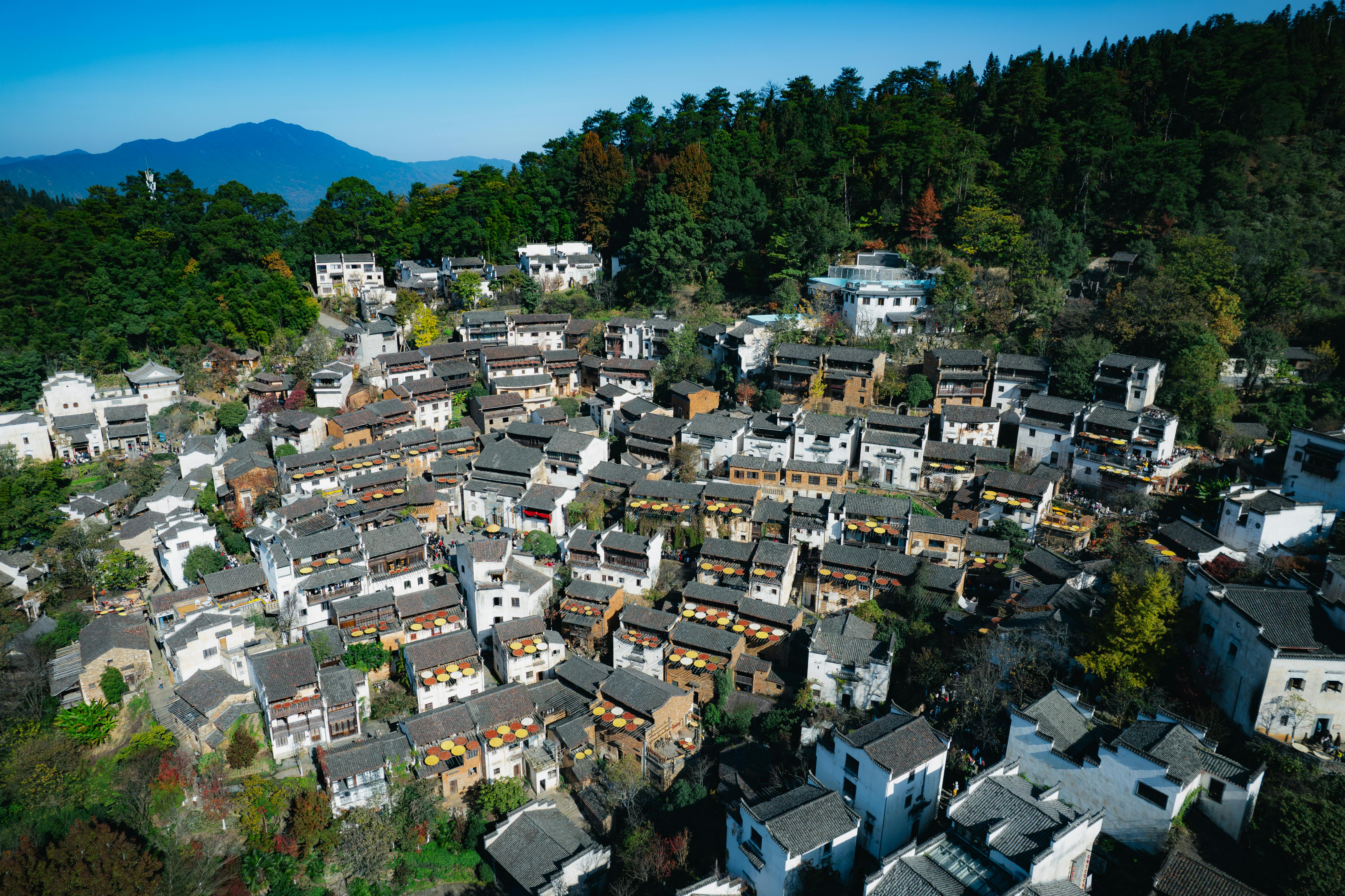 Aerial view of a traditional Chinese village surrounded by lush forests and distant mountains.