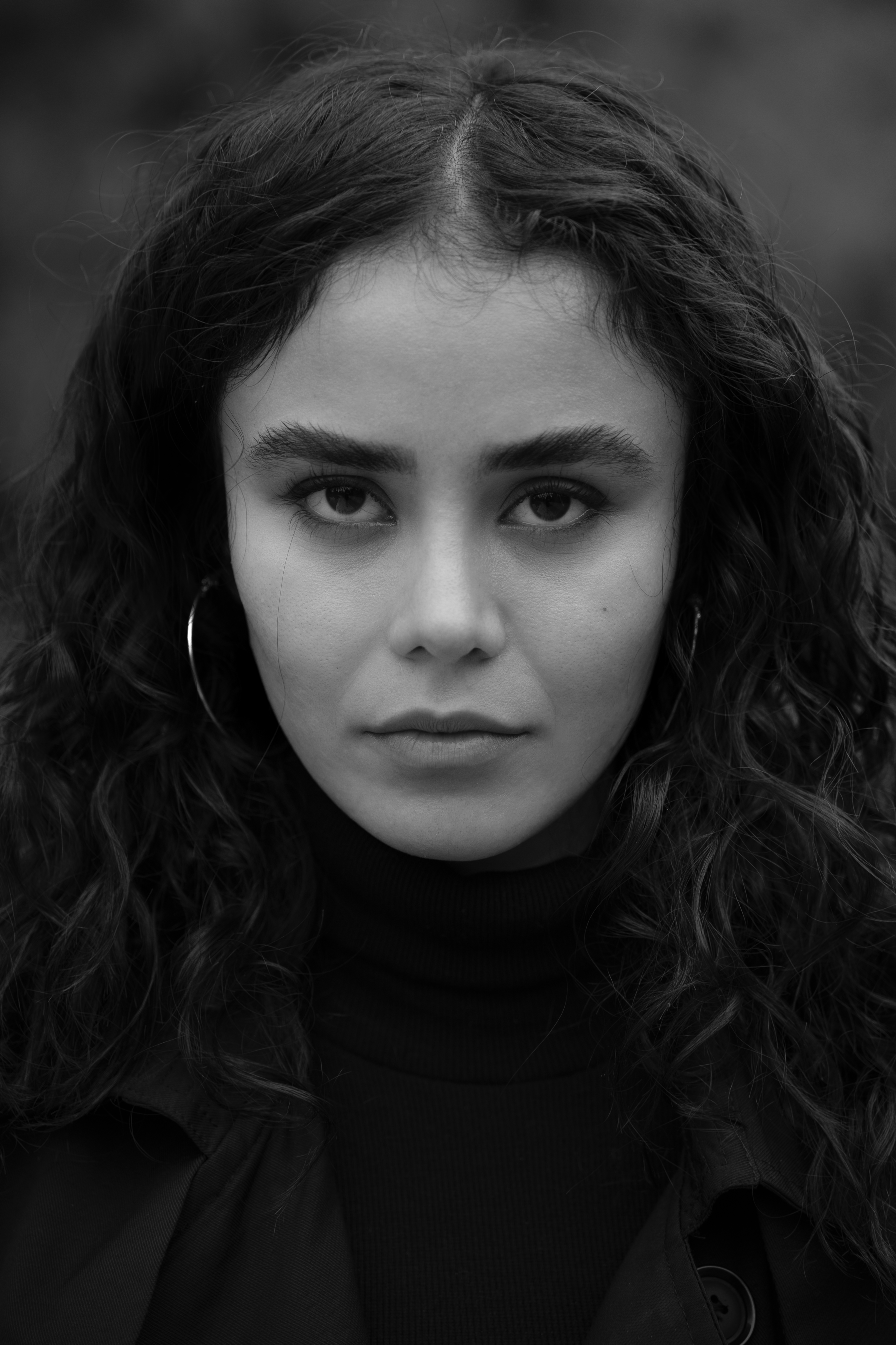 Striking black and white portrait of a young woman with curly hair and hoop earrings.
