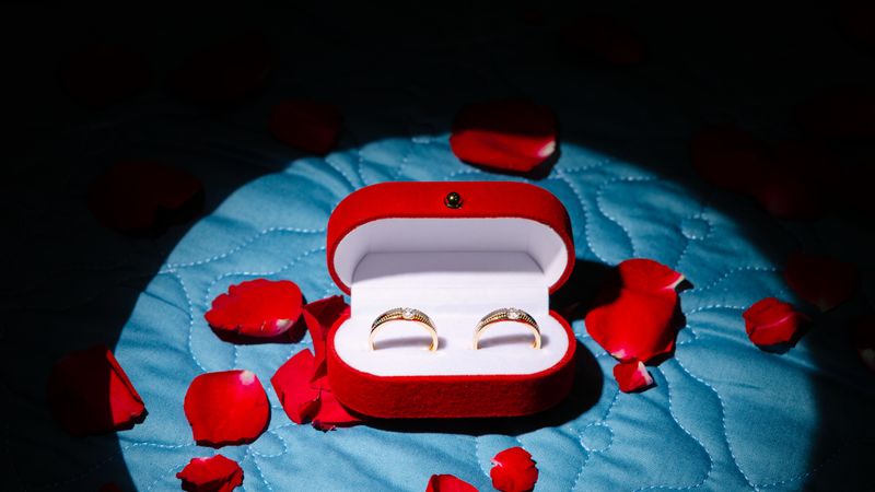 Elegantly designed wedding rings in a velvet box surrounded by rose petals.