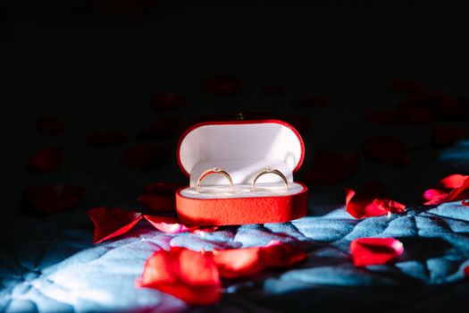A pair of gold rings inside a red velvet box surrounded by rose petals, symbolizing romance.