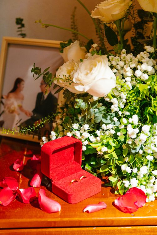 Free A beautiful wedding ring in a velvet box surrounded by white flowers and red petals, creating a romantic setting. Stock Photo