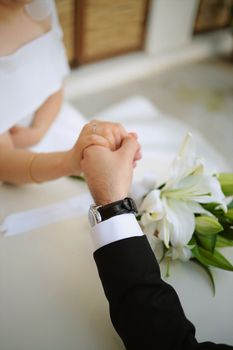 Close-up of a couple holding hands at a wedding ceremony with white lilies.