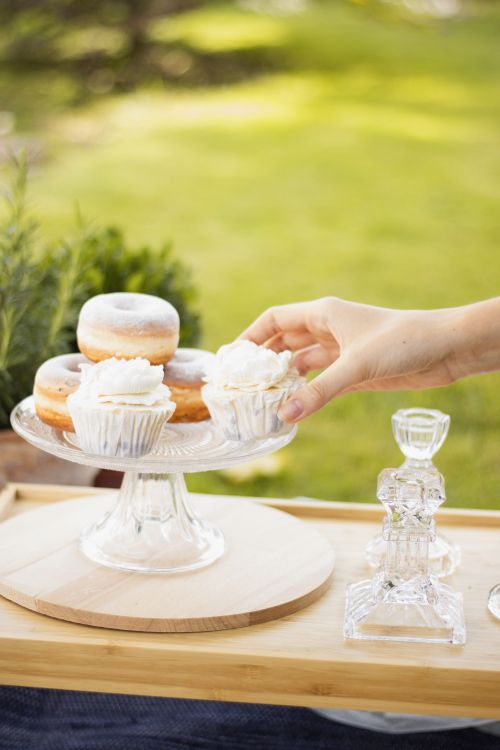 Free A hand reaching for cupcakes in a beautifully set outdoor scene with greenery. Stock Photo