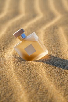 A chic perfume bottle nestled on sunlit sand with gentle waves texture in İstanbul.