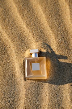 A stylish perfume bottle resting on golden sand under sunlight, evoking a luxurious vibe.