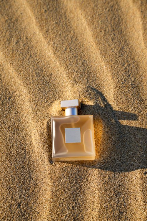 Free A stylish perfume bottle resting on golden sand under sunlight, evoking a luxurious vibe. Stock Photo