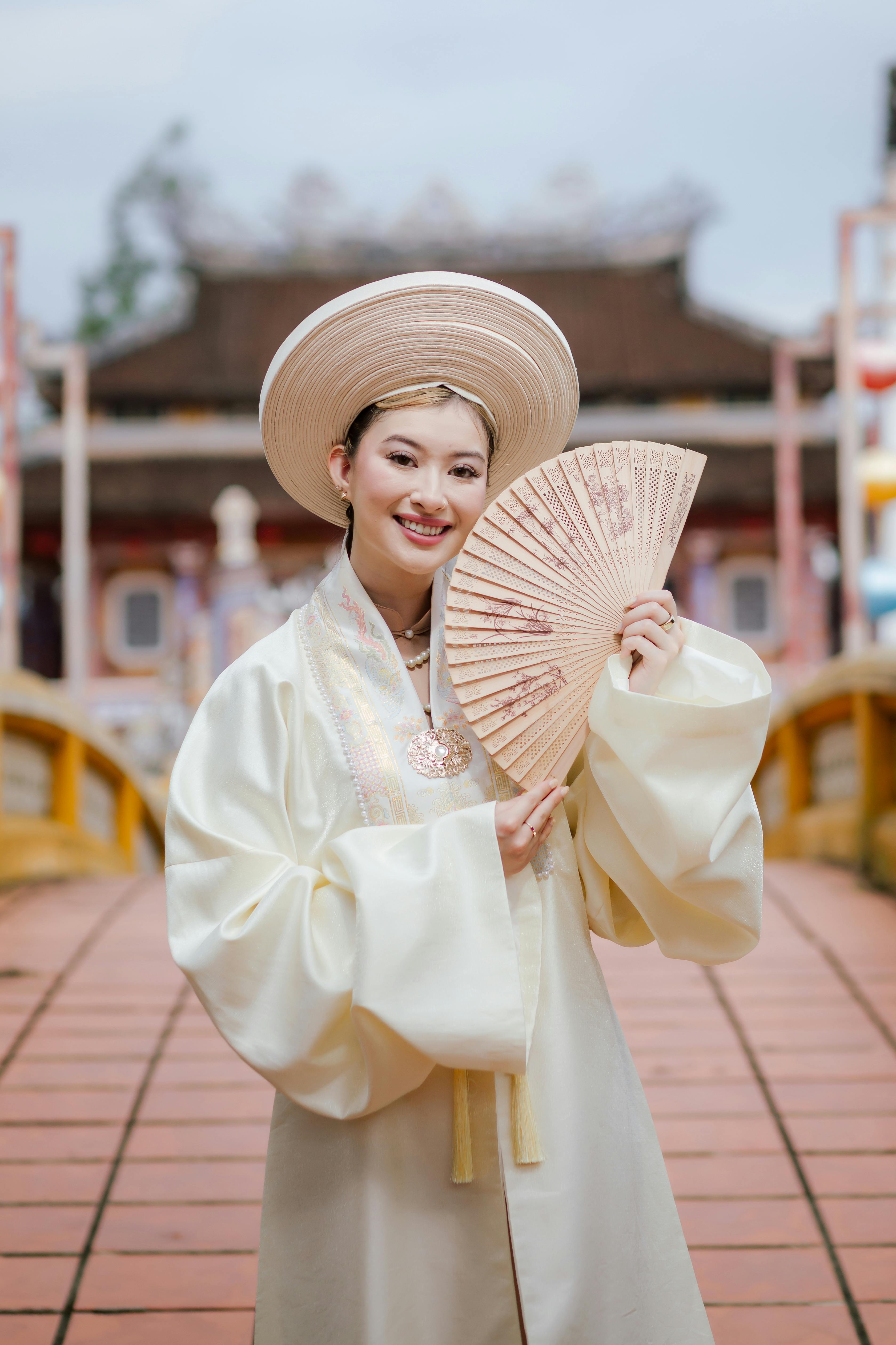 Woman in traditional Ao Dai holding fan on Hội An bridge, Vietnam.