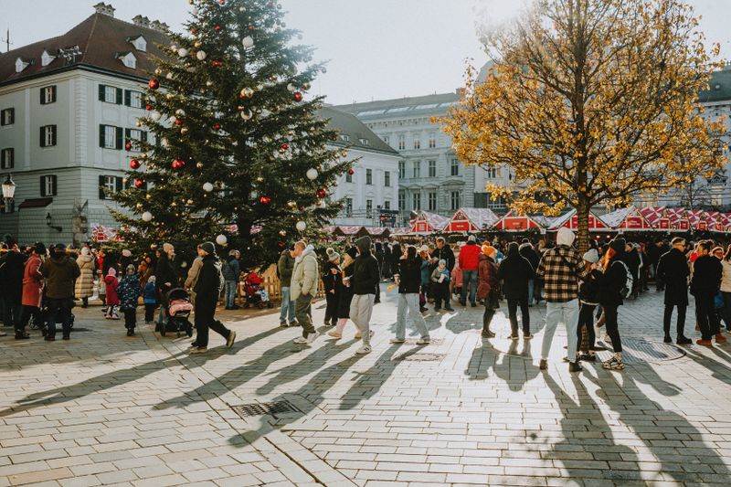 Târg de Crăciun într-o piață europeană cu brad mare și lumini festive